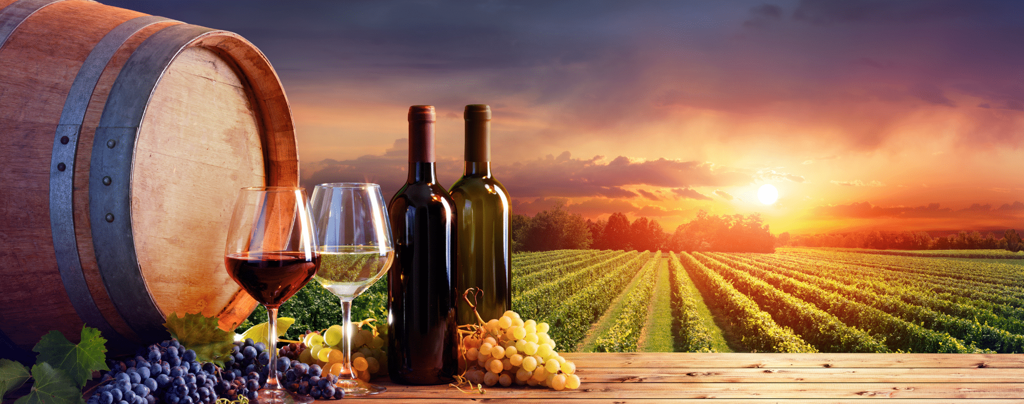 Wine bottles, glasses, and grapes are arranged on a wooden table with a vineyard backdrop at sunset, highlighting the beauty of wine culture.