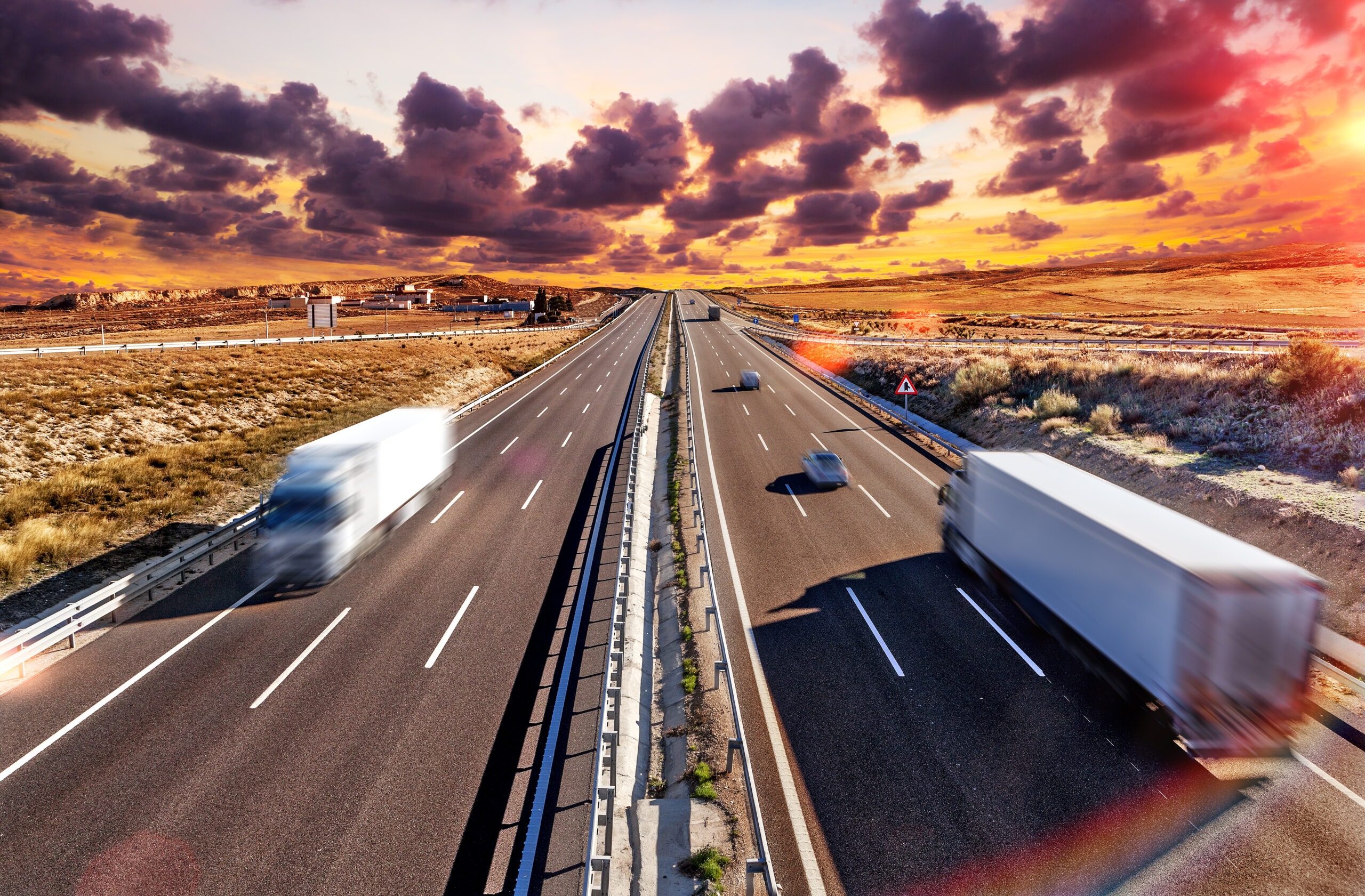 Highway scene at sunset, featuring moving vehicles and dramatic clouds. The image emphasizes transportation and roadway dynamics.