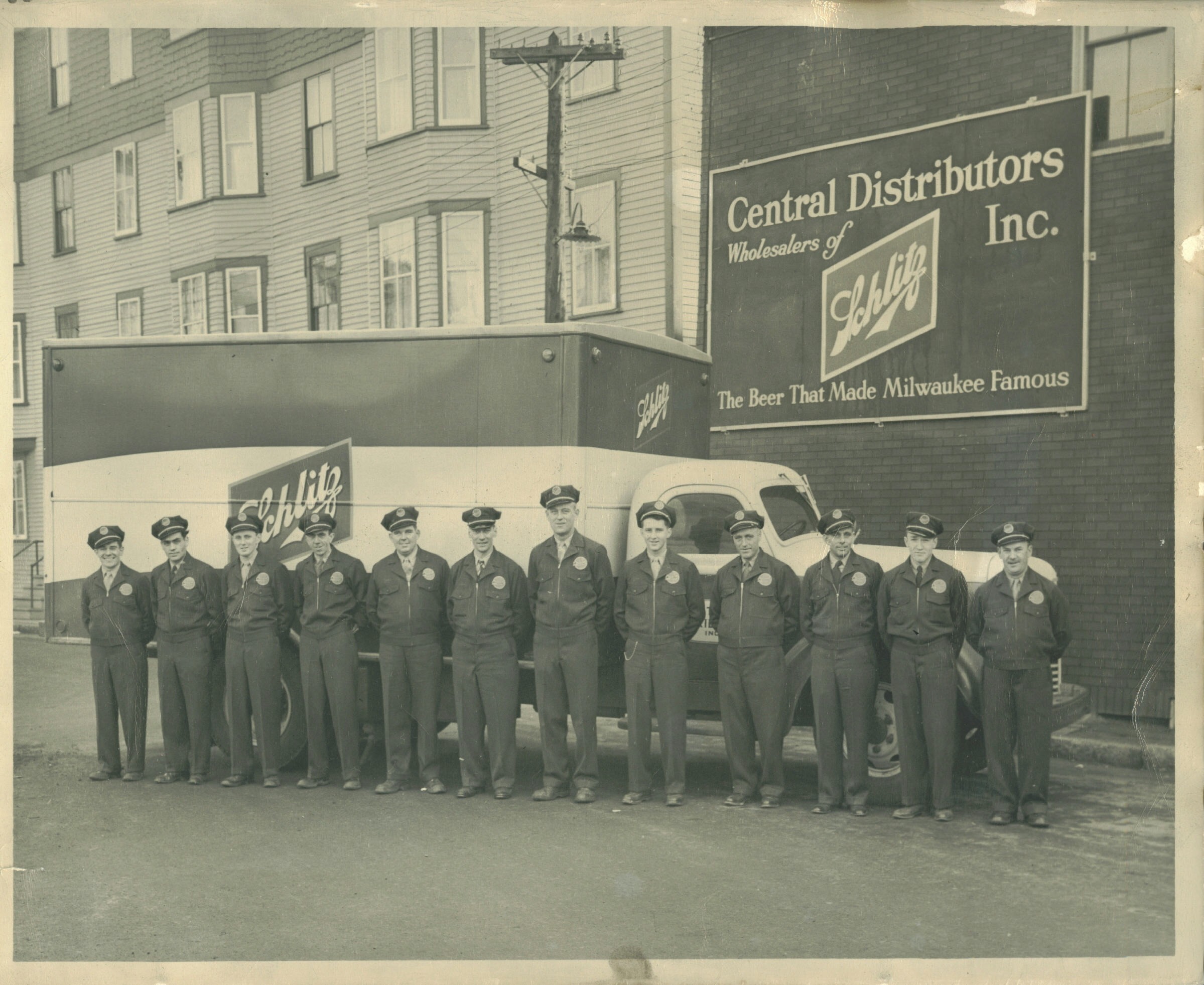 Schlitz beer distributors stand in front of a delivery truck, showcasing their branding. The photo highlights a historical moment in Milwaukee's brewing culture.